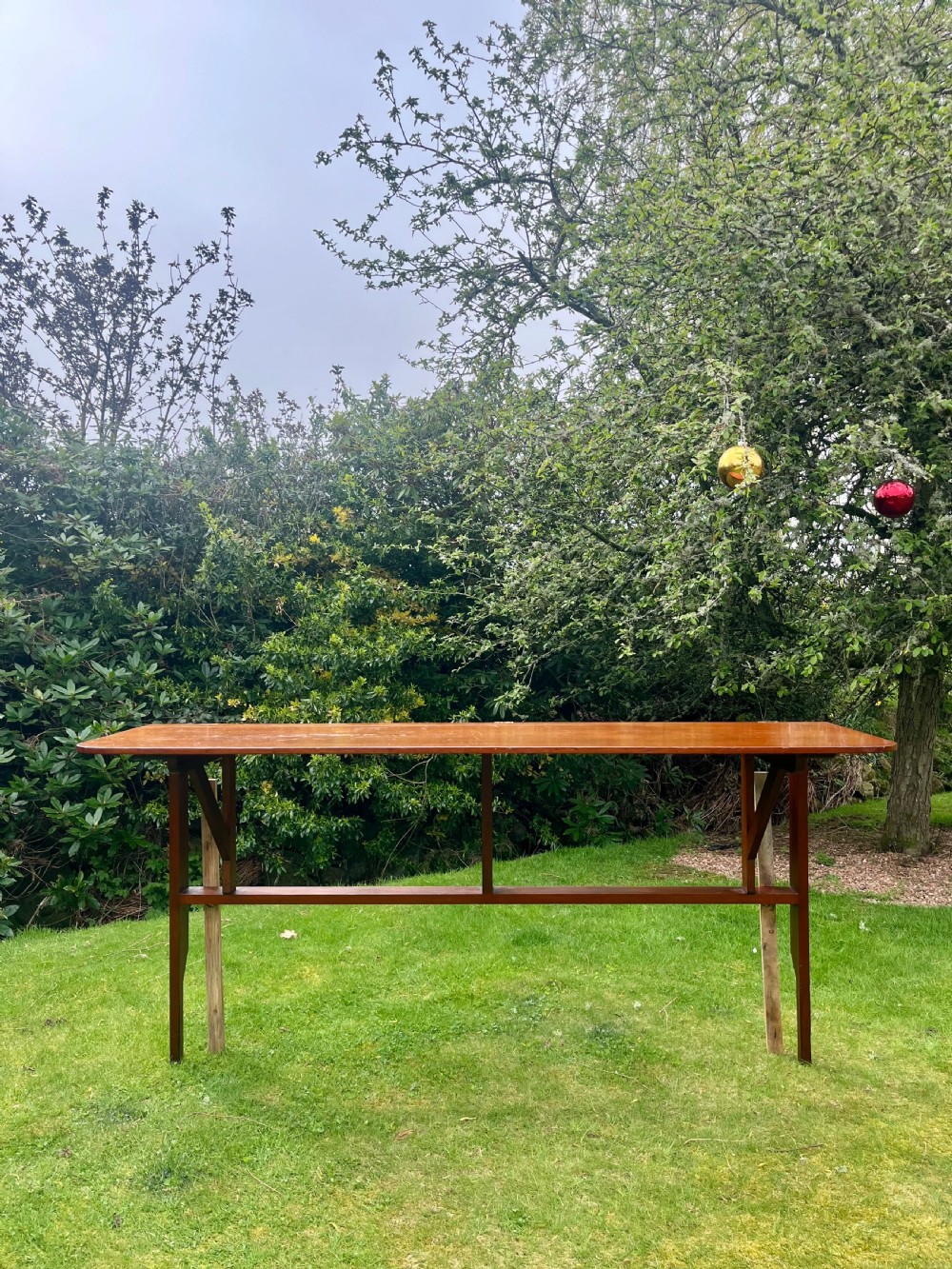 A long, narrow antique wooden butlers console table with a polished warm brown finish, rounded corners, and a collapsible trestle leg frame. View XIV