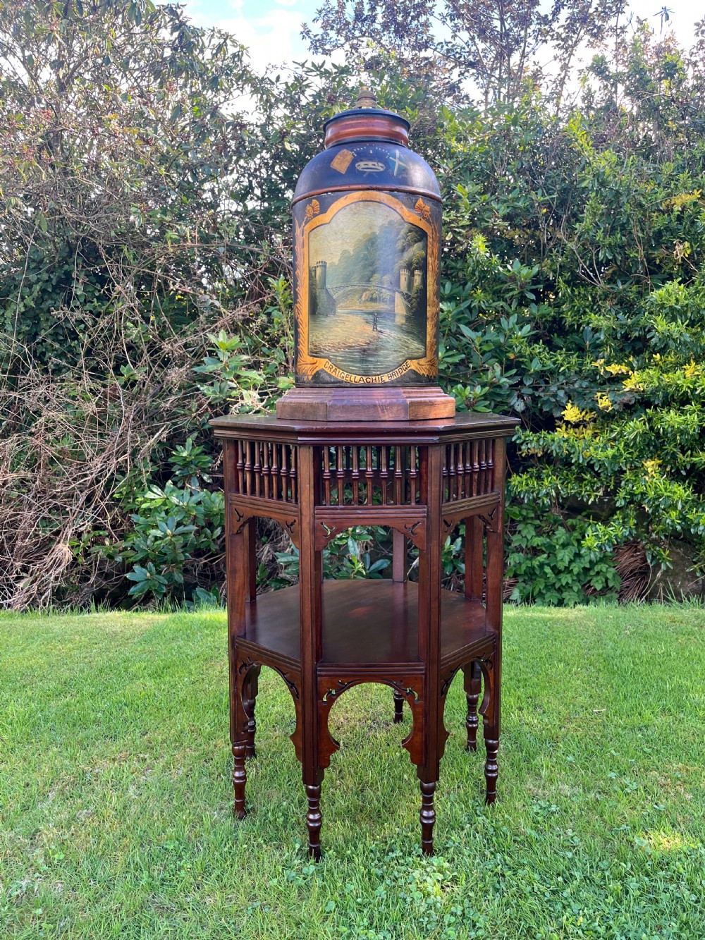 An antique dark metal tea canister converted into a table lamp, decorated with a hand-painted scene depicting Craigellachie Bridge set on a wooden base. View II