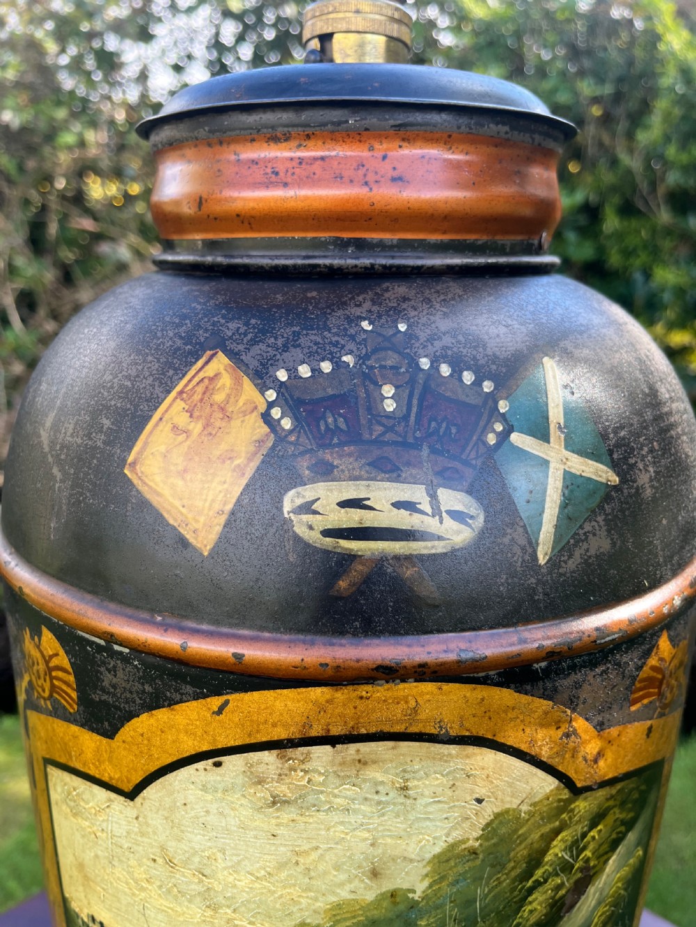 An antique dark metal tea canister converted into a table lamp, decorated with a hand-painted scene depicting Craigellachie Bridge set on a wooden base. View V