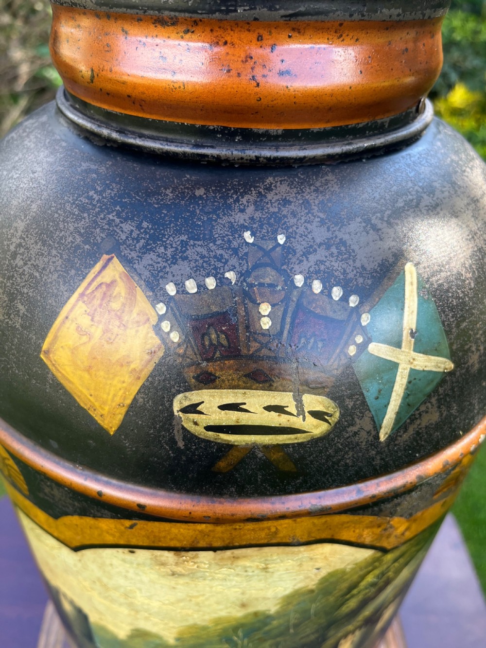 An antique dark metal tea canister converted into a table lamp, decorated with a hand-painted scene depicting Craigellachie Bridge set on a wooden base. View X