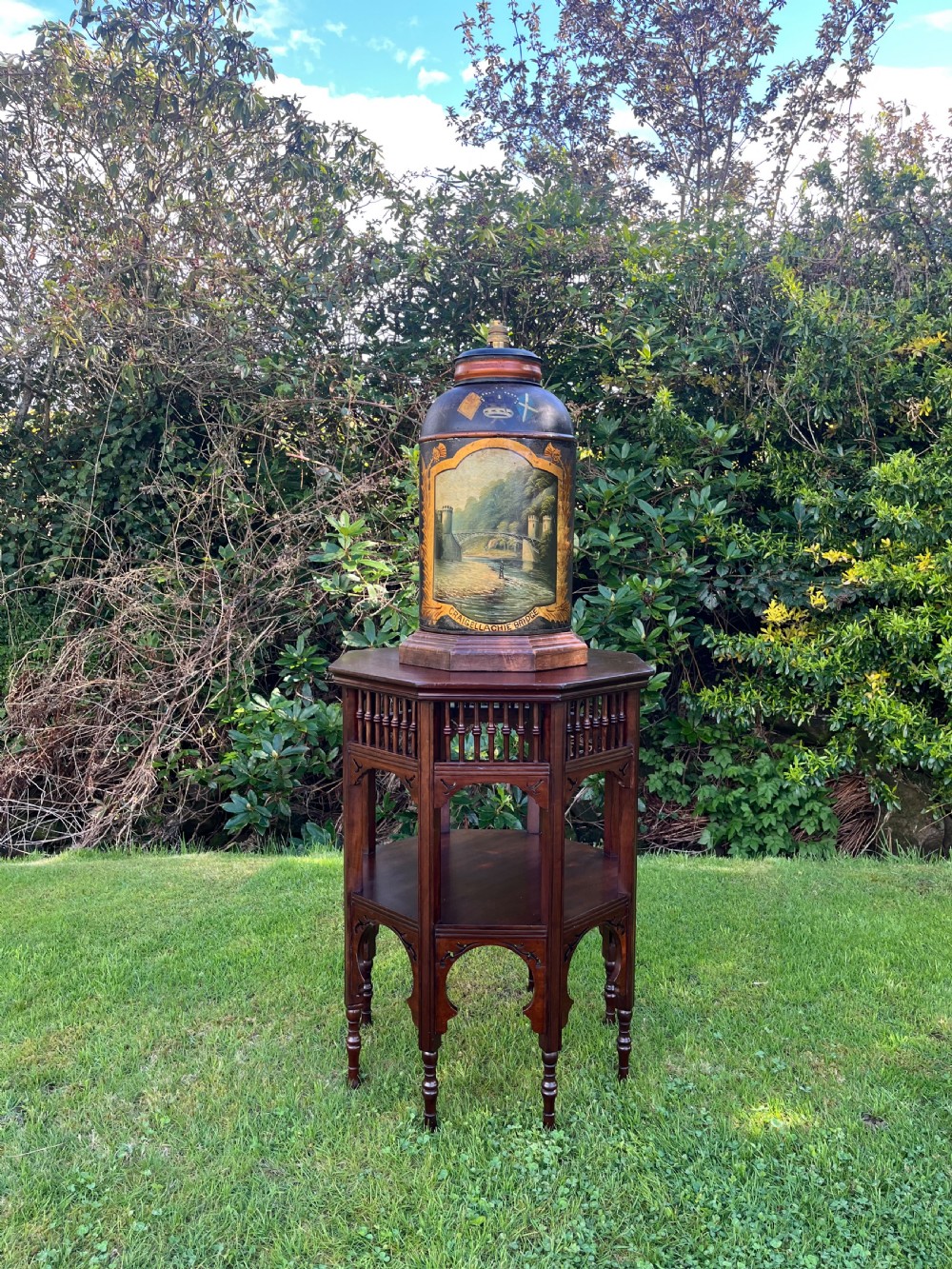 An antique dark metal tea canister converted into a table lamp, decorated with a hand-painted scene depicting Craigellachie Bridge set on a wooden base. View XIV