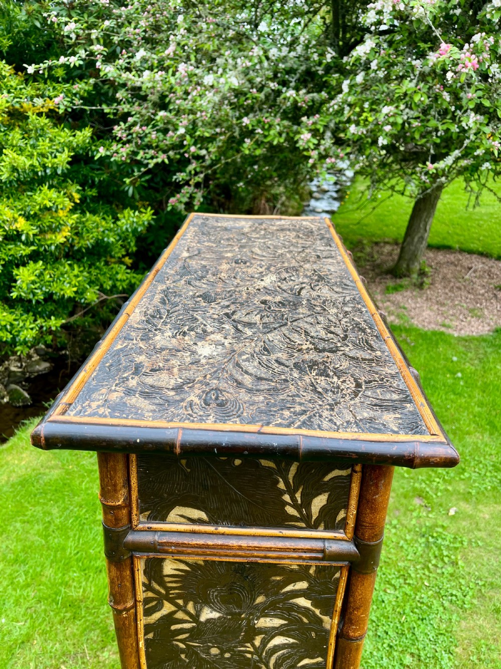 A late Victorian bamboo display cabinet with two glazed doors, upper drawers, and dark embossed botanical pattern panels. View II