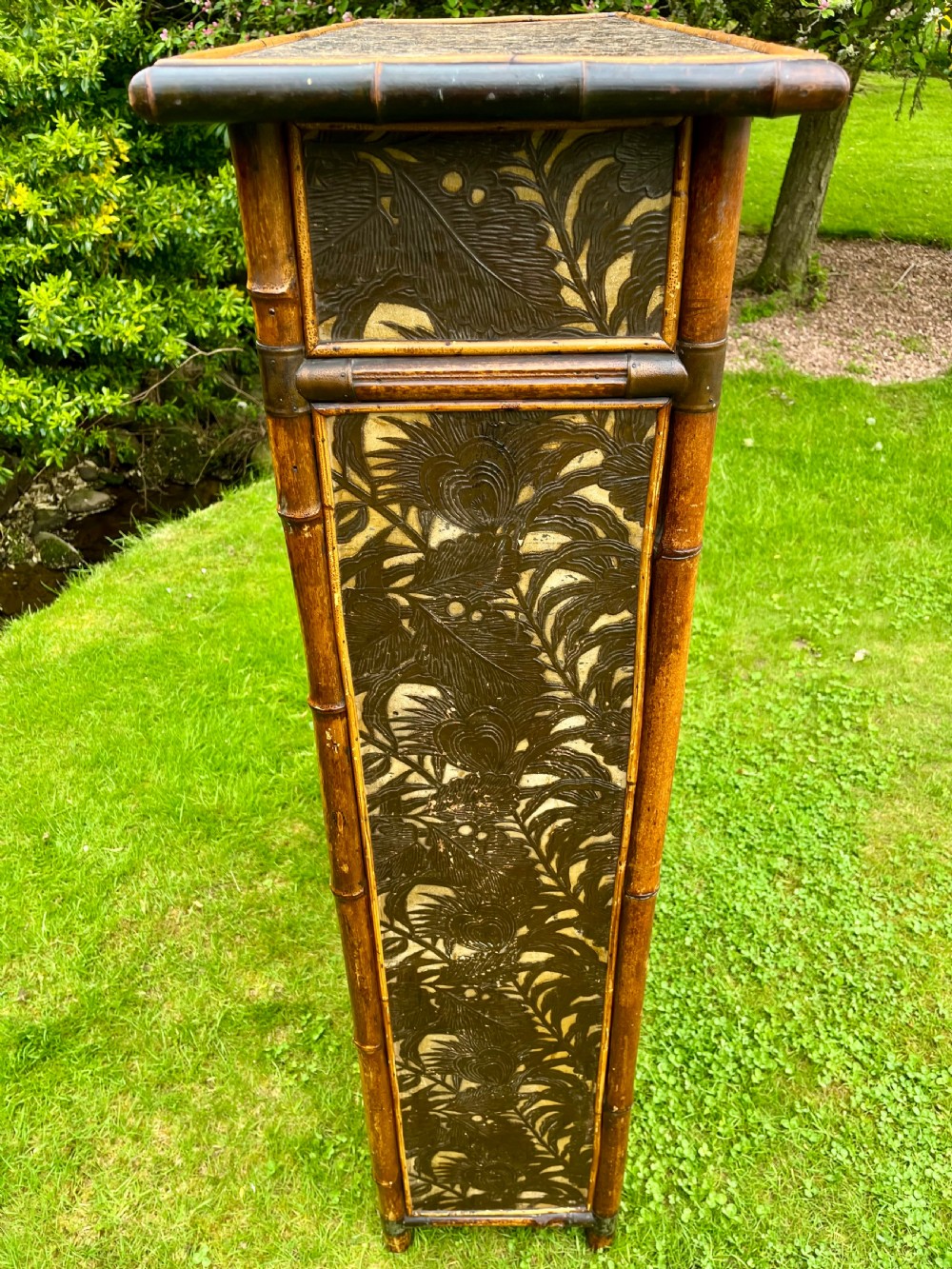 A late Victorian bamboo display cabinet with two glazed doors, upper drawers, and dark embossed botanical pattern panels. View IV