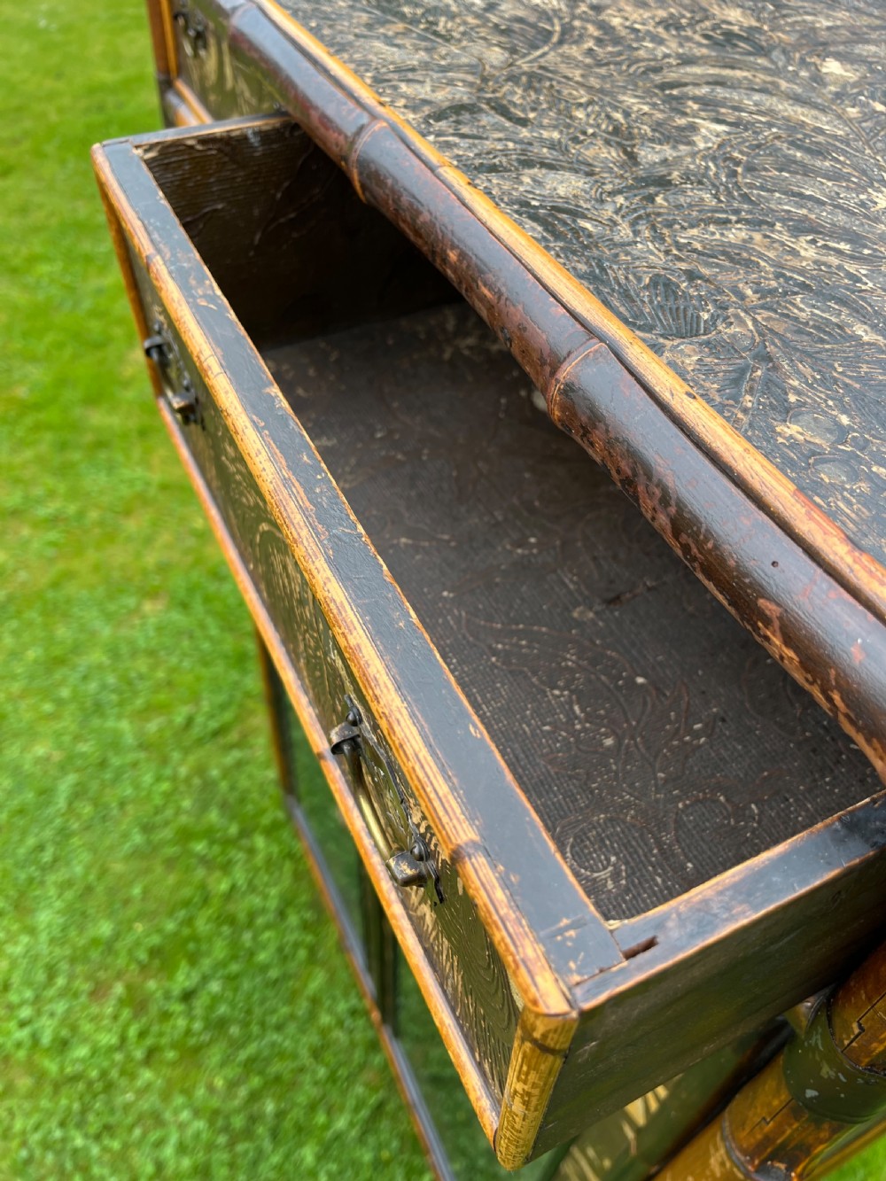 A late Victorian bamboo display cabinet with two glazed doors, upper drawers, and dark embossed botanical pattern panels. View V