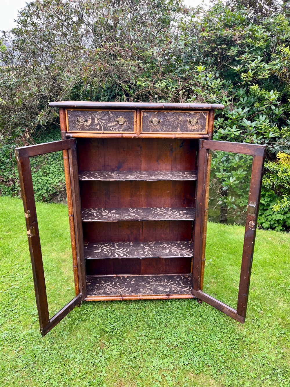 A late Victorian bamboo display cabinet with two glazed doors, upper drawers, and dark embossed botanical pattern panels. View VIII
