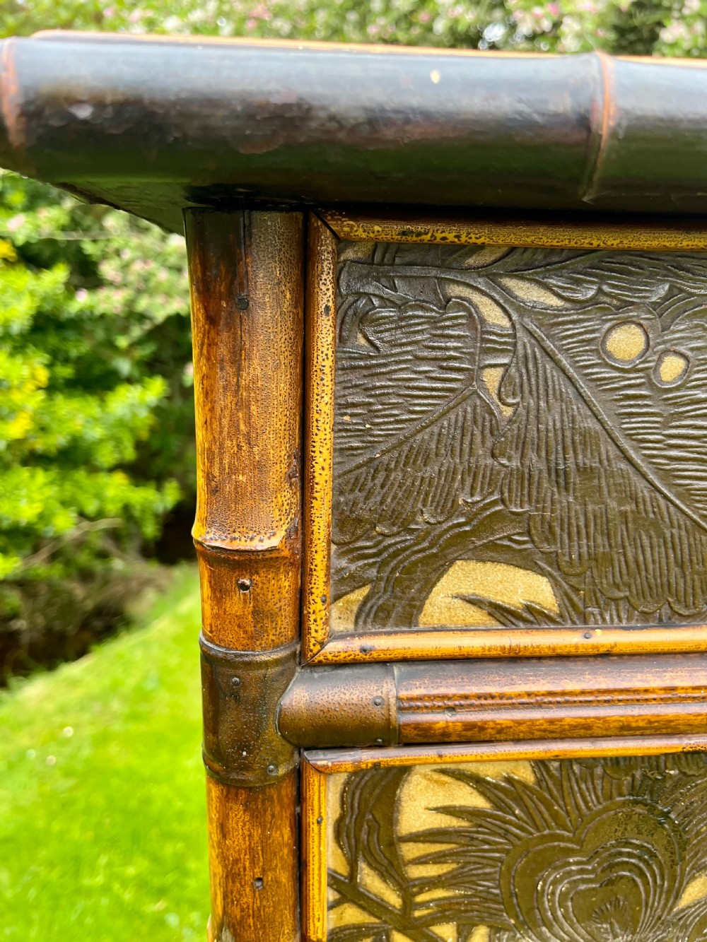 A late Victorian bamboo display cabinet with two glazed doors, upper drawers, and dark embossed botanical pattern panels. View XII