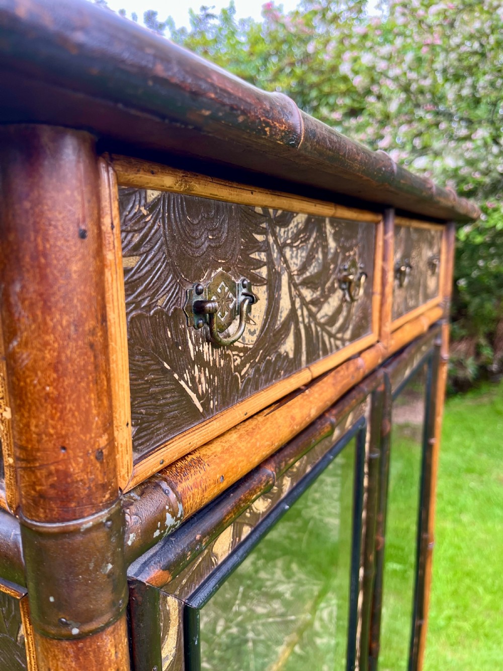 A late Victorian bamboo display cabinet with two glazed doors, upper drawers, and dark embossed botanical pattern panels. View XVI