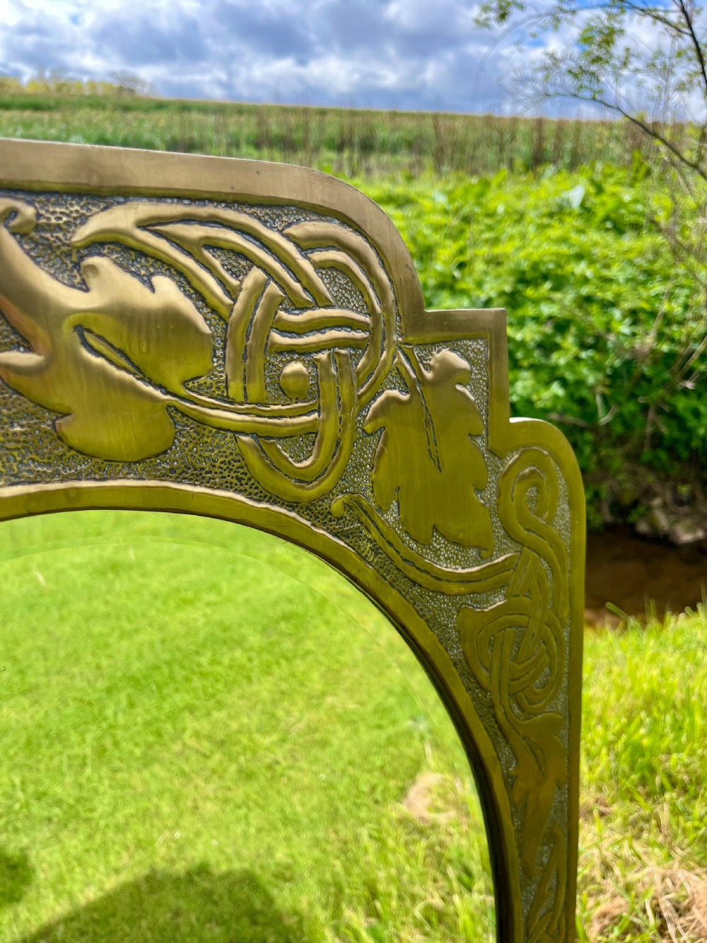 A large shaped brass wall mirror featuring an oval glass centre enclosed by relief Celtic knotwork and leaf motifs. View II