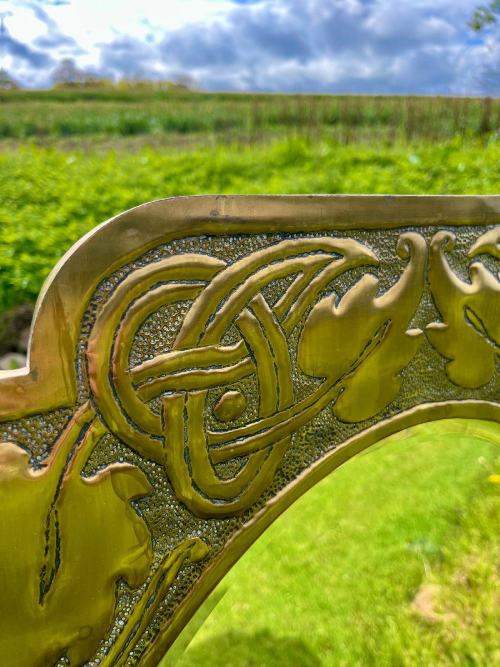 A large shaped brass wall mirror featuring an oval glass centre enclosed by relief Celtic knotwork and leaf motifs. View III