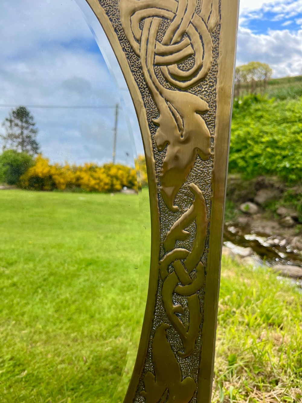 A large shaped brass wall mirror featuring an oval glass centre enclosed by relief Celtic knotwork and leaf motifs. View IV