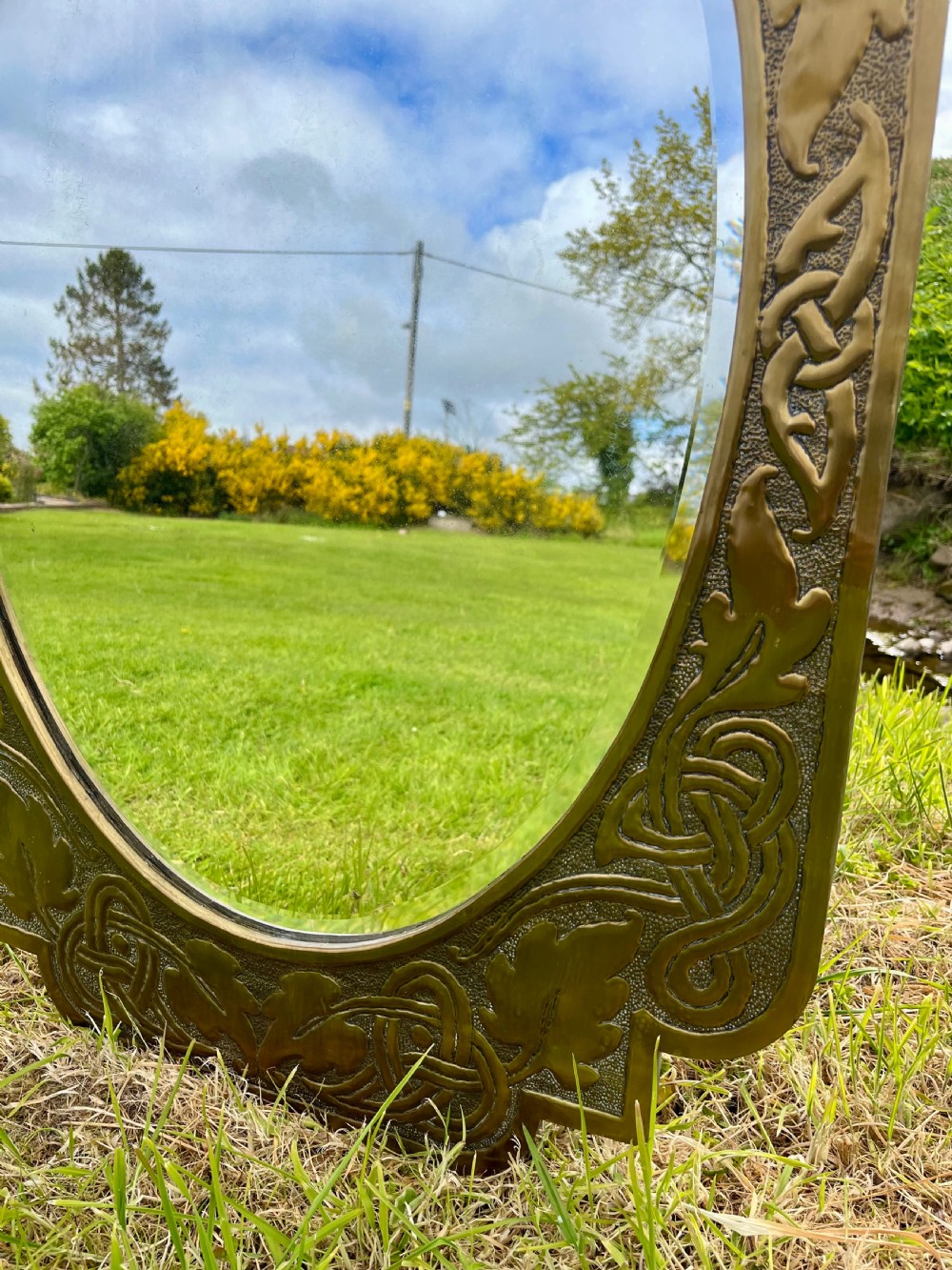 A large shaped brass wall mirror featuring an oval glass centre enclosed by relief Celtic knotwork and leaf motifs. View V
