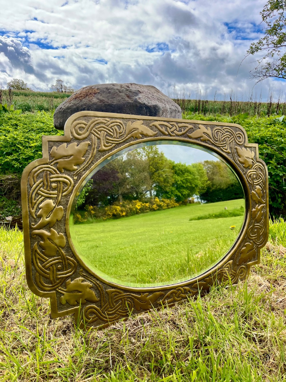 A large shaped brass wall mirror featuring an oval glass centre enclosed by relief Celtic knotwork and leaf motifs. View VI