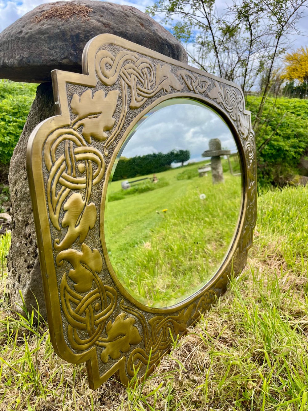 A large shaped brass wall mirror featuring an oval glass centre enclosed by relief Celtic knotwork and leaf motifs. View X