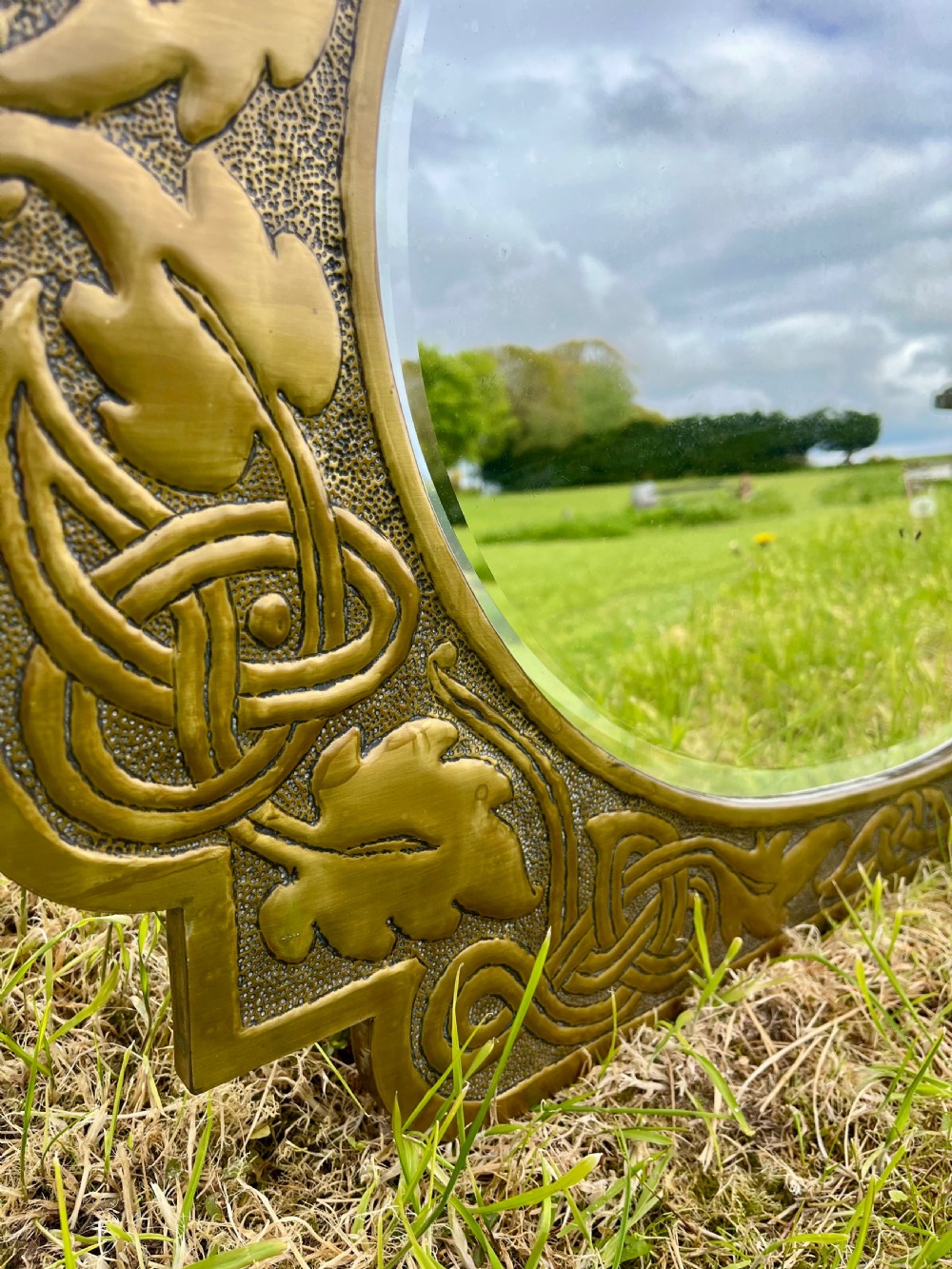 A large shaped brass wall mirror featuring an oval glass centre enclosed by relief Celtic knotwork and leaf motifs. View XI