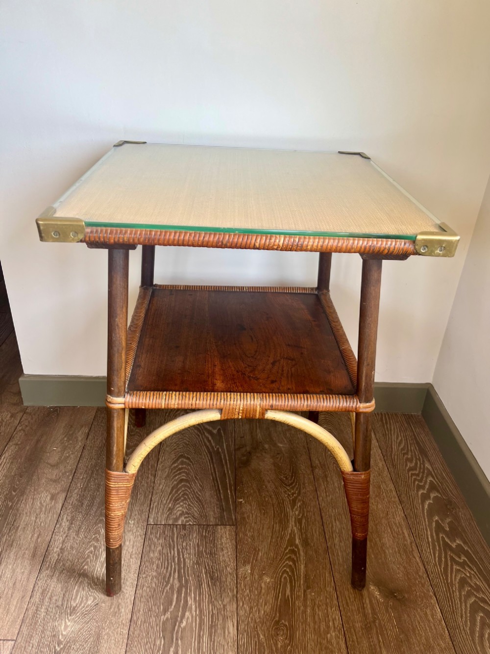 A square two-tier Dryad cane occasional table with a clear glass top, brass corner mounts, dark wood lower shelf, and woven tapered legs.