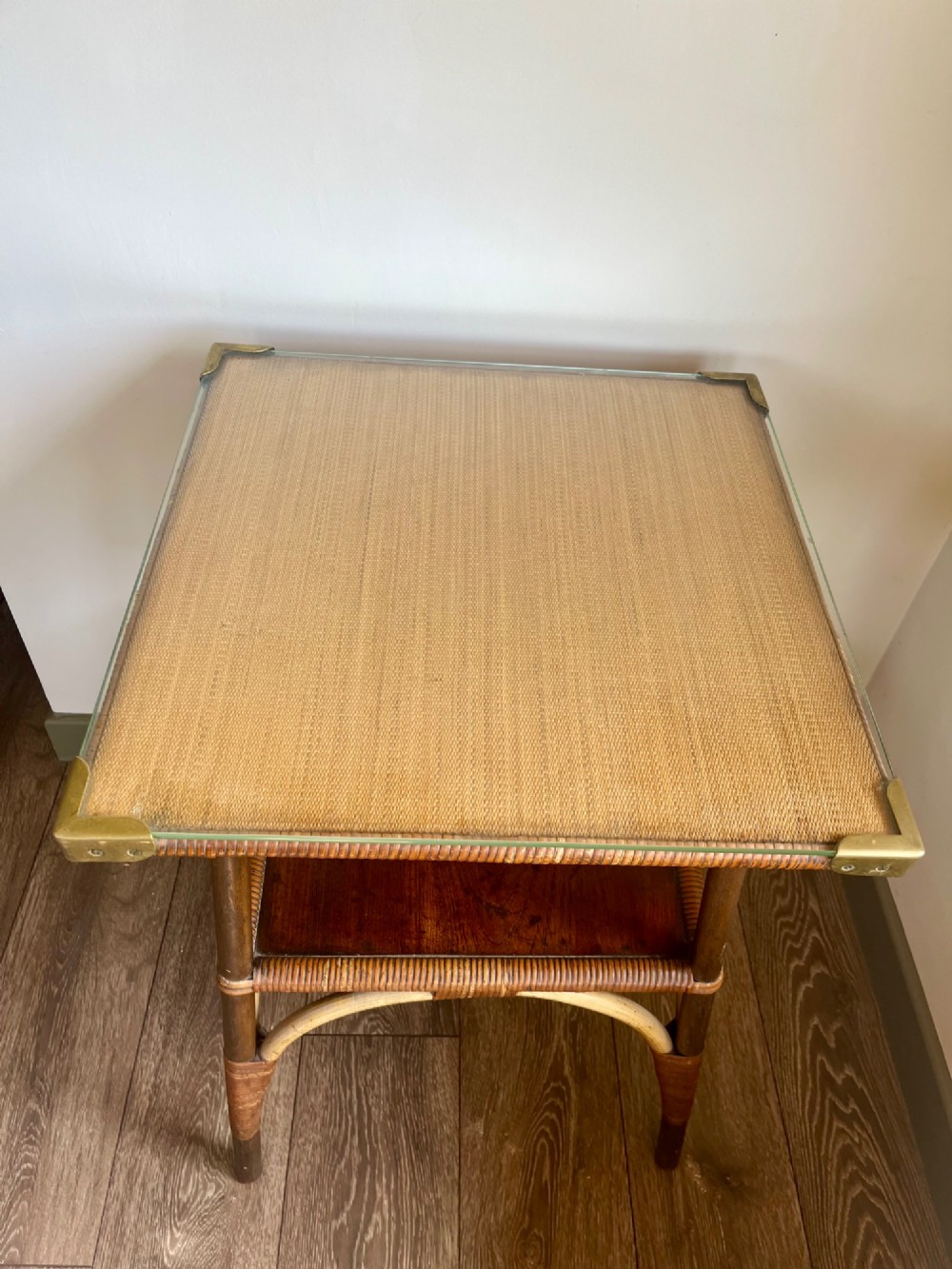 A square two-tier Dryad cane occasional table with a clear glass top, brass corner mounts, dark wood lower shelf, and woven tapered legs. View V