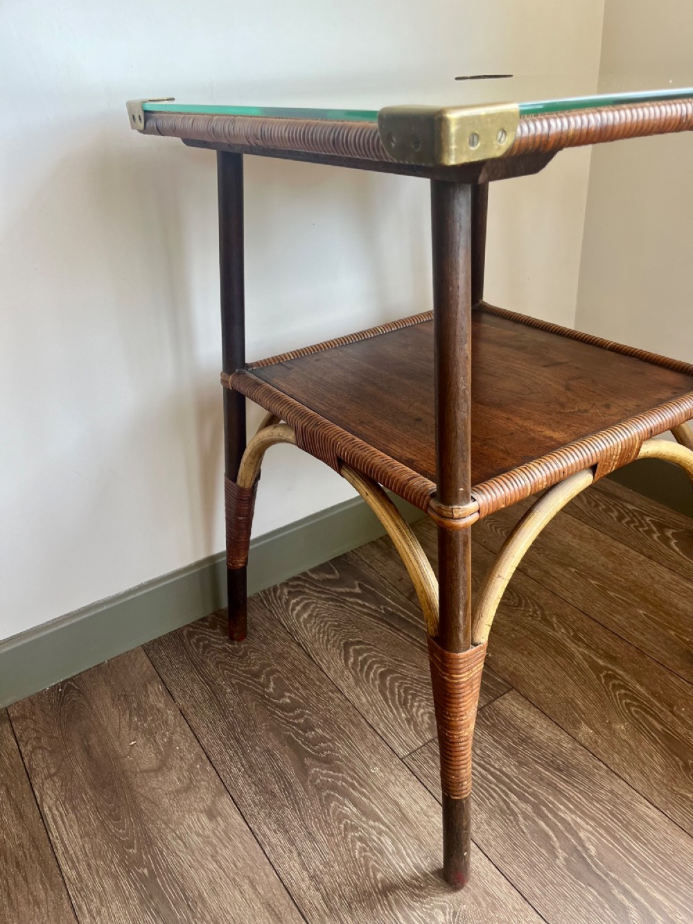 A square two-tier Dryad cane occasional table with a clear glass top, brass corner mounts, dark wood lower shelf, and woven tapered legs. View VI