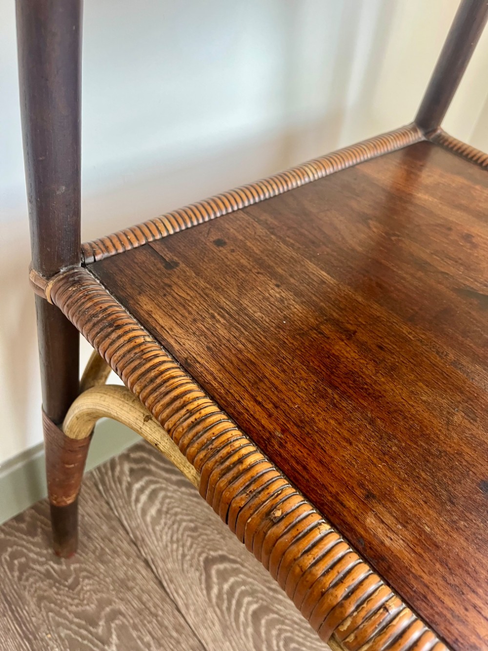 A square two-tier Dryad cane occasional table with a clear glass top, brass corner mounts, dark wood lower shelf, and woven tapered legs. View VII