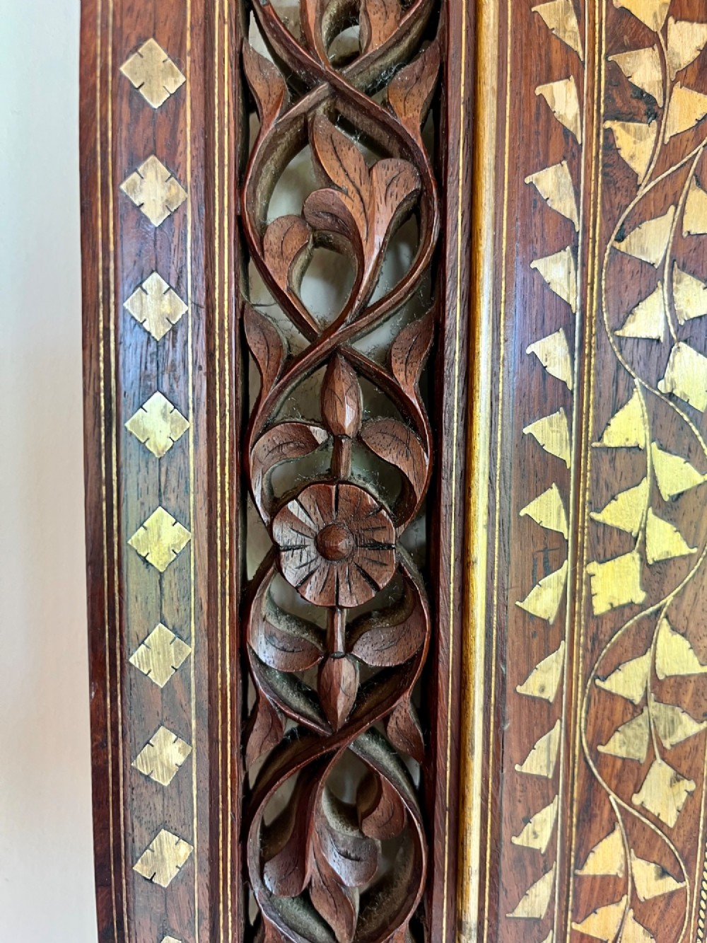 Corner detail of a rectangular dark wood frame decorated with brass foliate inlay and pierced scrollwork panels. View II