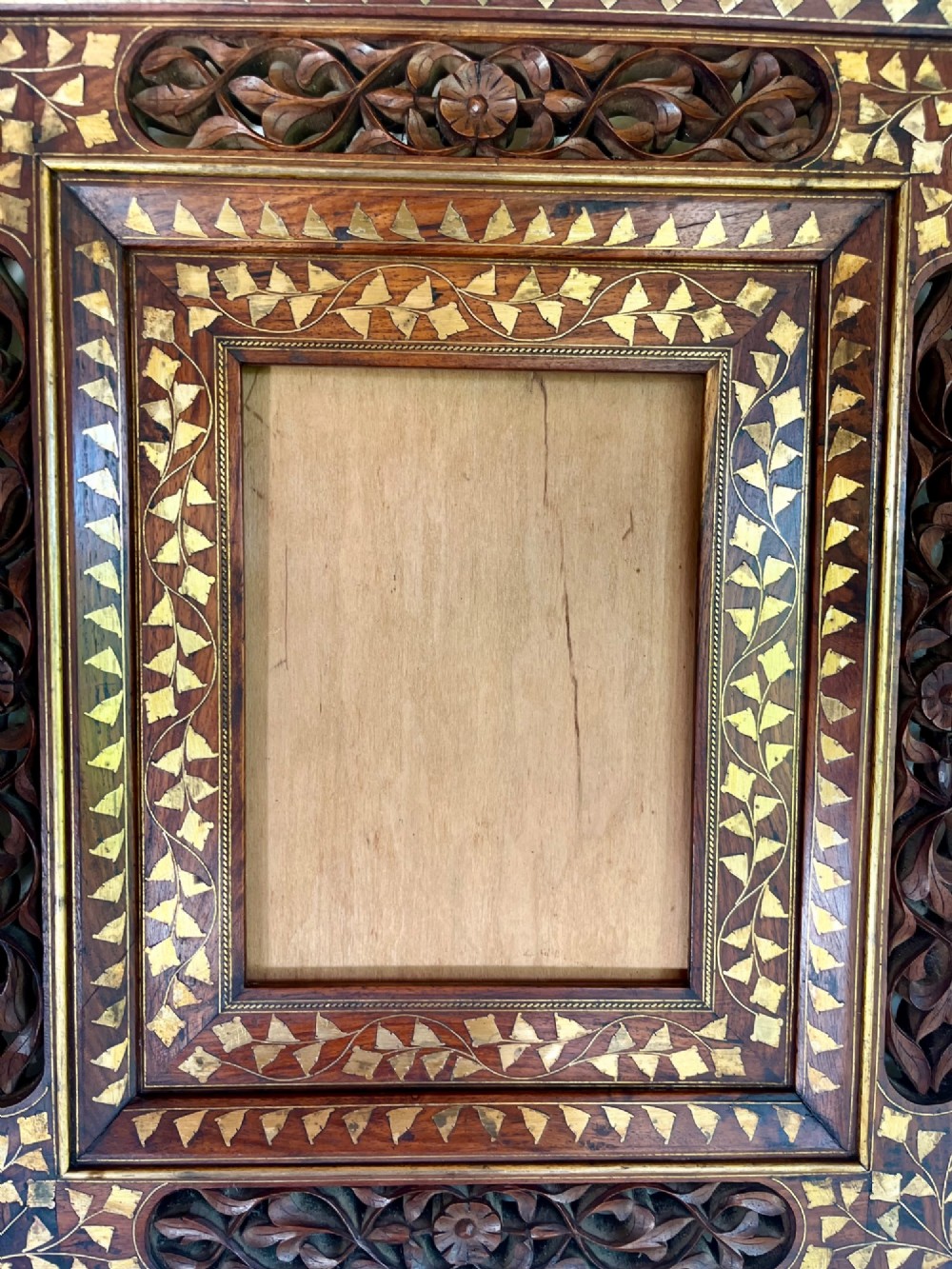Corner detail of a rectangular dark wood frame decorated with brass foliate inlay and pierced scrollwork panels. View IV