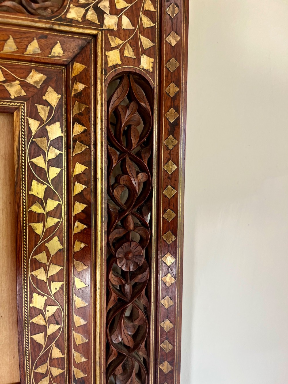 Corner detail of a rectangular dark wood frame decorated with brass foliate inlay and pierced scrollwork panels. View V