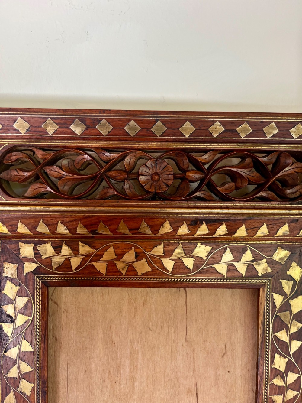 Corner detail of a rectangular dark wood frame decorated with brass foliate inlay and pierced scrollwork panels. View VI