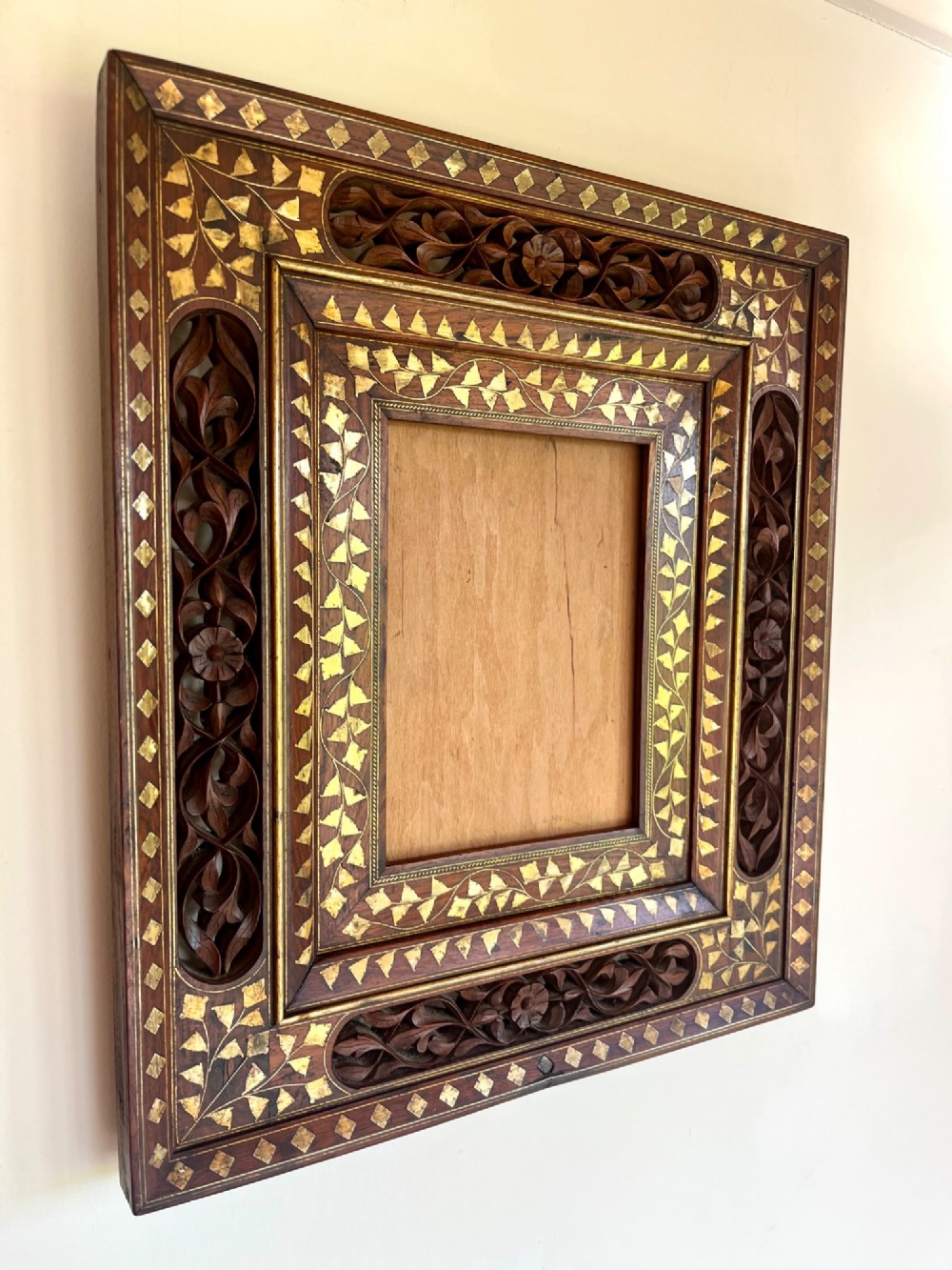 Corner detail of a rectangular dark wood frame decorated with brass foliate inlay and pierced scrollwork panels. View VII