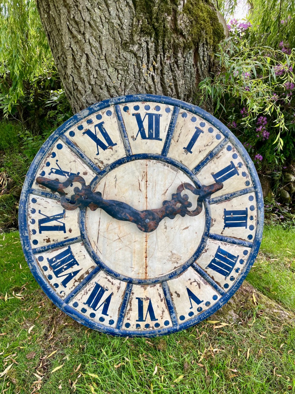 A circular antique French tower clock face with cream and blue painted sections, blue Roman numerals, and decorative wrought iron hands.