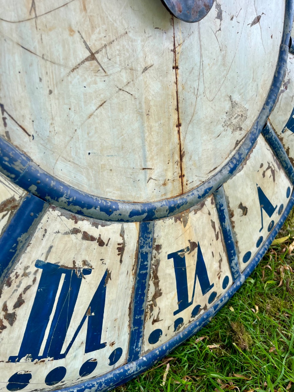 A circular antique French tower clock face with cream and blue painted sections, blue Roman numerals, and decorative wrought iron hands. View V