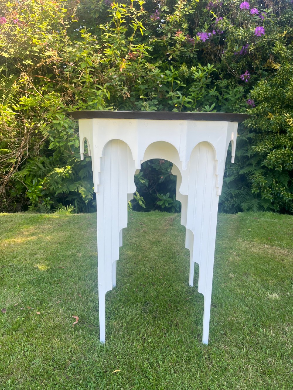 A white painted Moorish style occasional table featuring stepped horseshoe arches and a dark contrasting tray top.