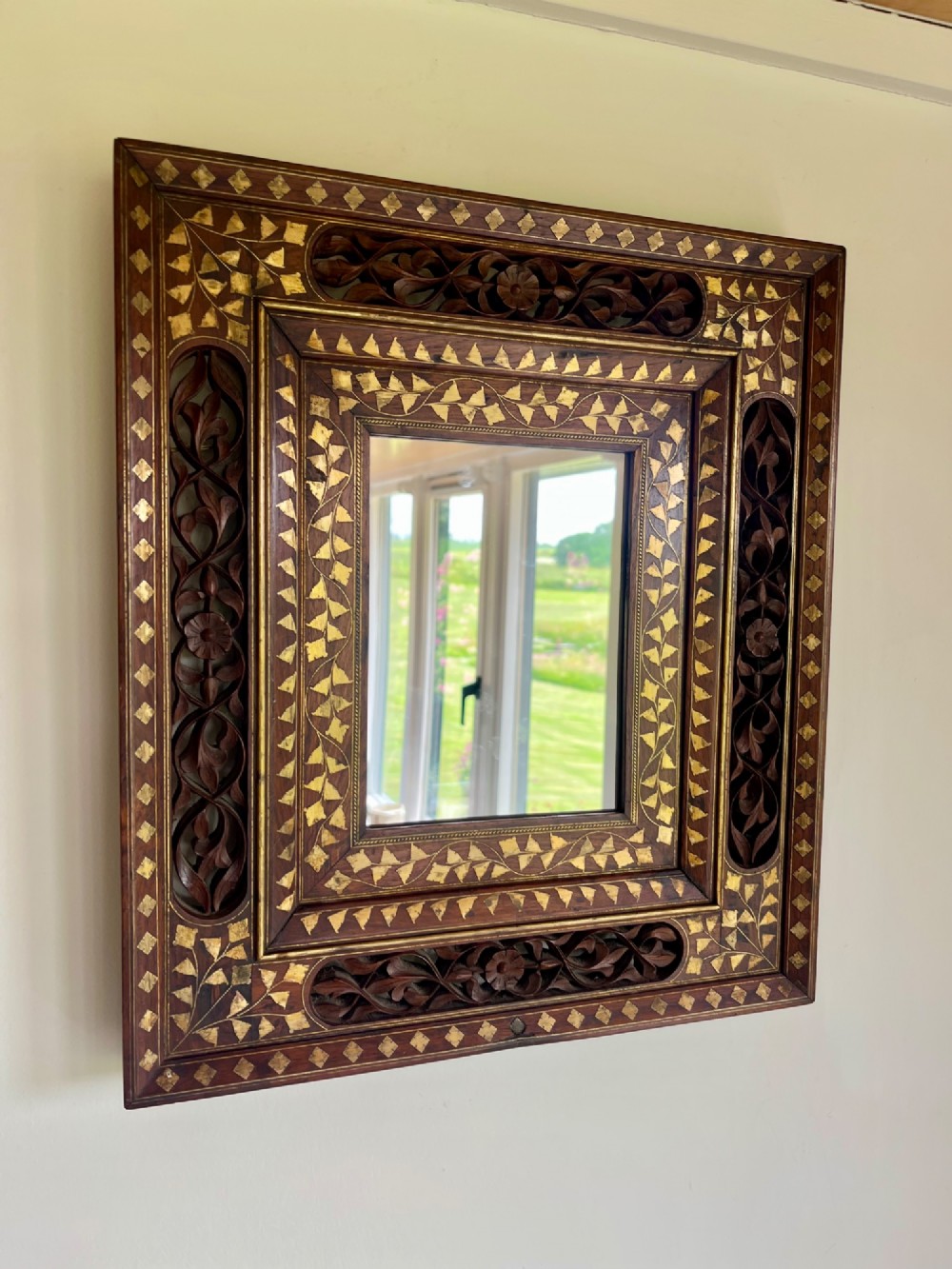 Corner detail of a rectangular dark wood frame decorated with brass foliate inlay and pierced scrollwork panels. View XI
