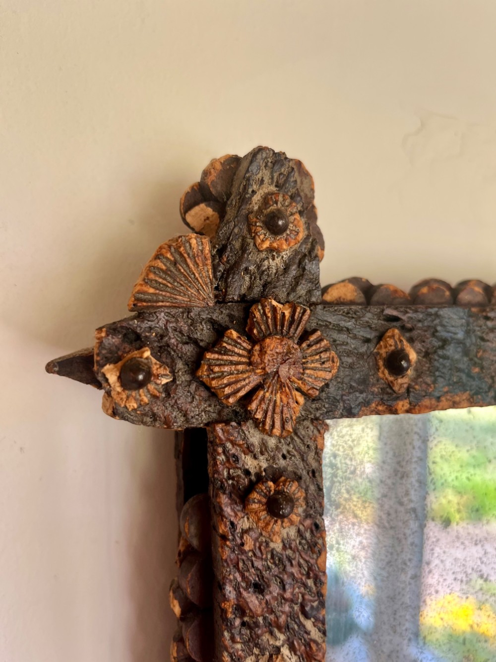 A square antique wall mirror framed with layered dark cork bark featuring intricate hand-carved rosettes and geometric notched corners surrounding foxed mirror glass. View II