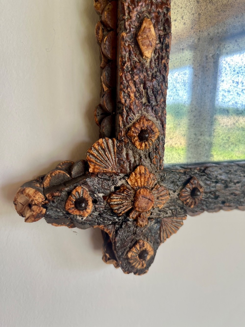 A square antique wall mirror framed with layered dark cork bark featuring intricate hand-carved rosettes and geometric notched corners surrounding foxed mirror glass. View III