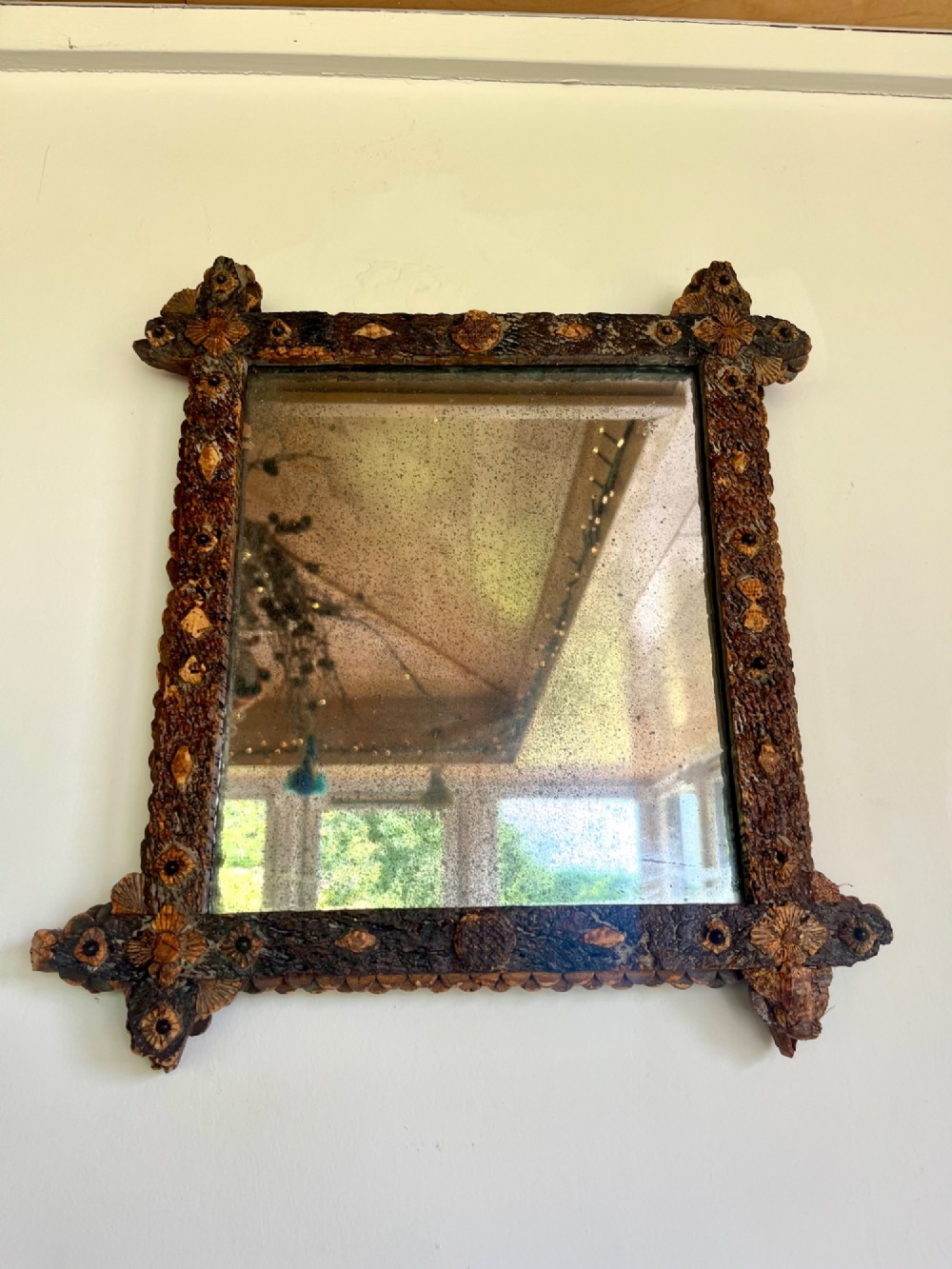 A square antique wall mirror framed with layered dark cork bark featuring intricate hand-carved rosettes and geometric notched corners surrounding foxed mirror glass. View IV