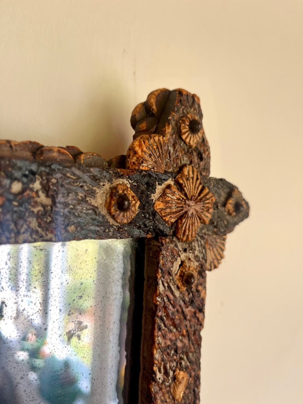 A square antique wall mirror framed with layered dark cork bark featuring intricate hand-carved rosettes and geometric notched corners surrounding foxed mirror glass. View V
