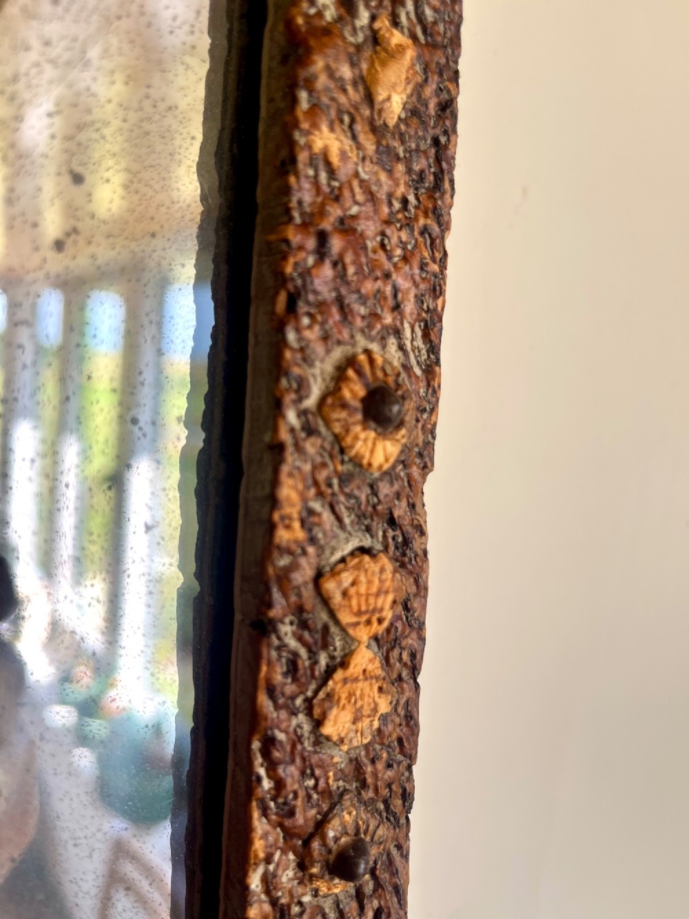 A square antique wall mirror framed with layered dark cork bark featuring intricate hand-carved rosettes and geometric notched corners surrounding foxed mirror glass. View VI
