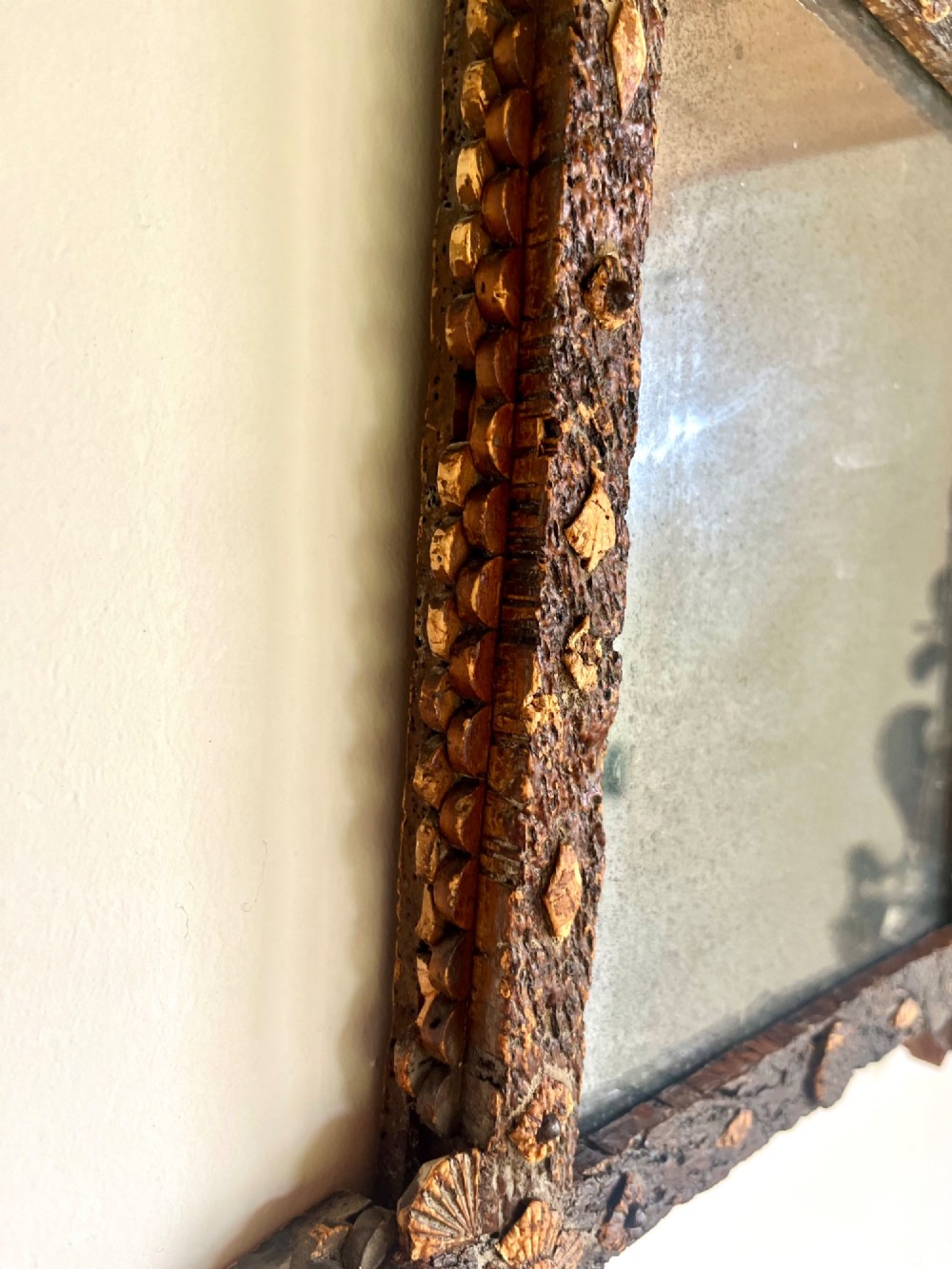 A square antique wall mirror framed with layered dark cork bark featuring intricate hand-carved rosettes and geometric notched corners surrounding foxed mirror glass. View VII