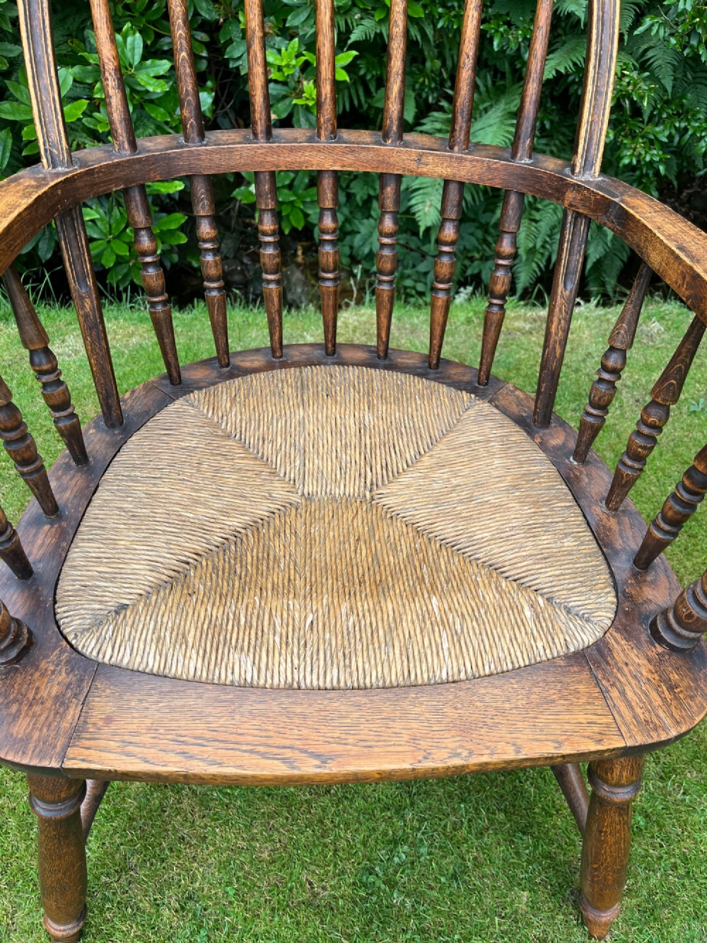An antique ash Windsor armchair featuring a hoop back with vertical spindles, curved armrests, a woven rush seat, and turned legs linked by stretchers. View II