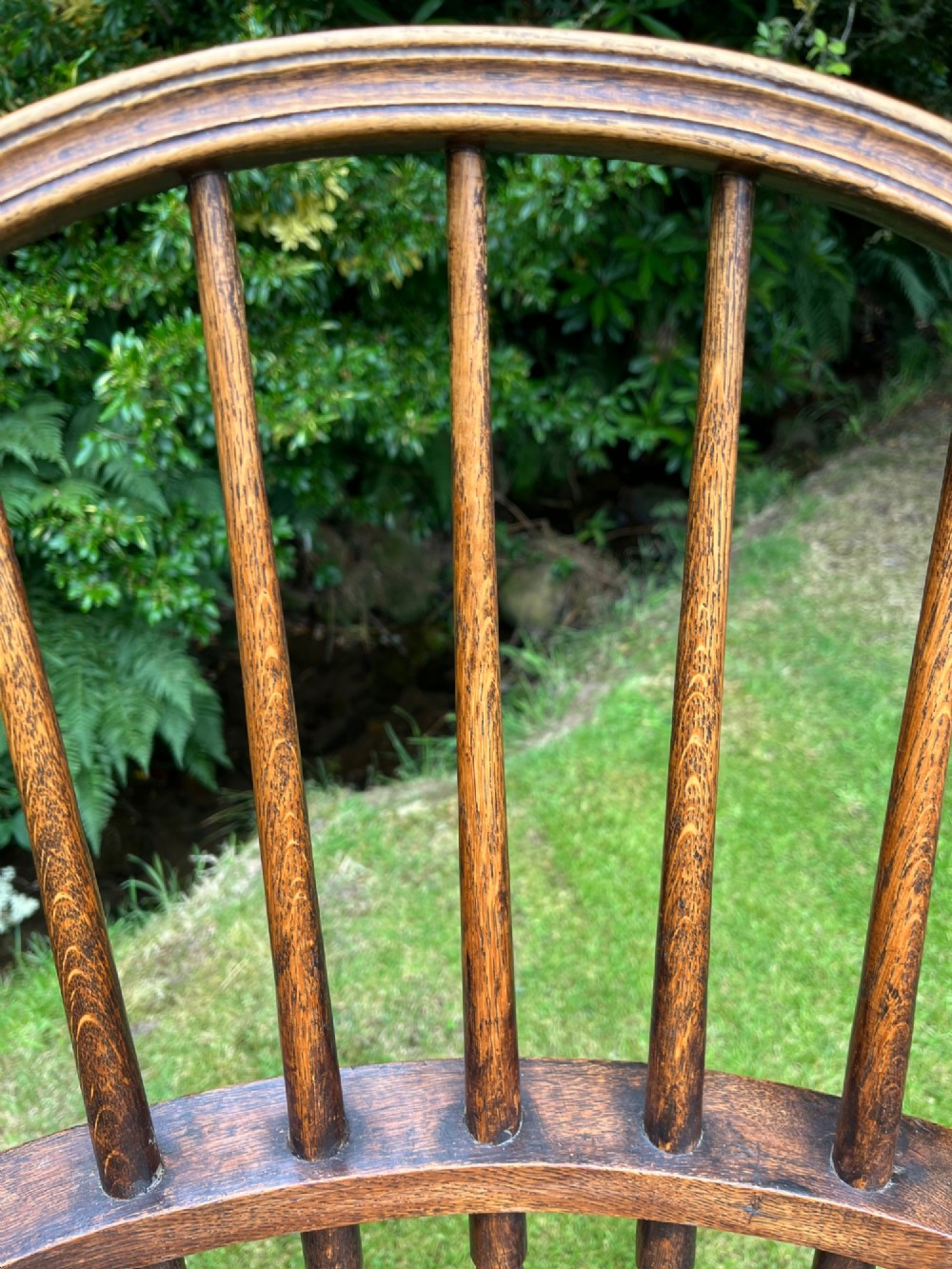 An antique ash Windsor armchair featuring a hoop back with vertical spindles, curved armrests, a woven rush seat, and turned legs linked by stretchers. View IV