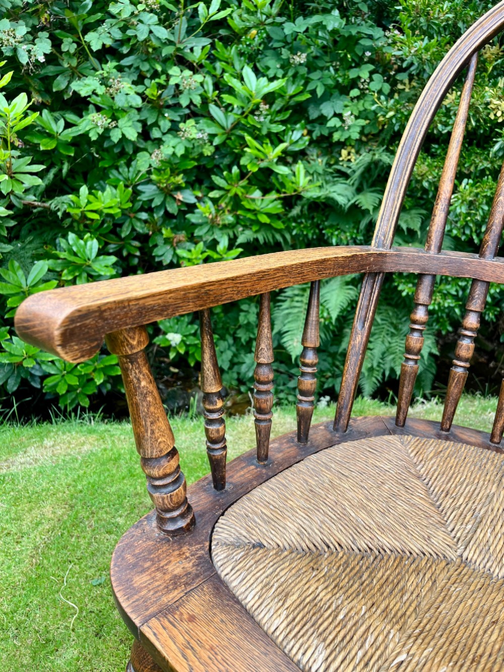 An antique ash Windsor armchair featuring a hoop back with vertical spindles, curved armrests, a woven rush seat, and turned legs linked by stretchers. View V