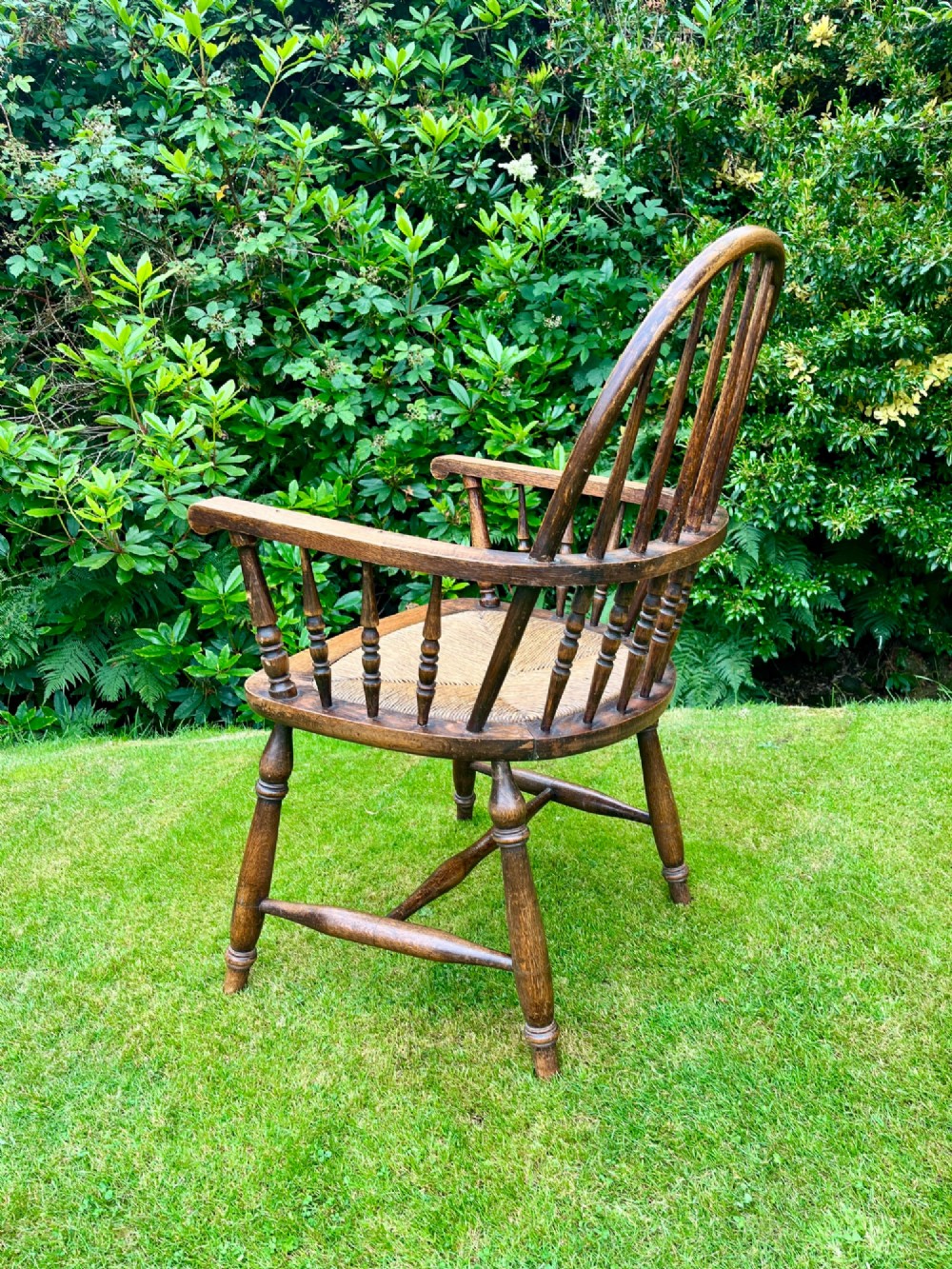 An antique ash Windsor armchair featuring a hoop back with vertical spindles, curved armrests, a woven rush seat, and turned legs linked by stretchers. View VI