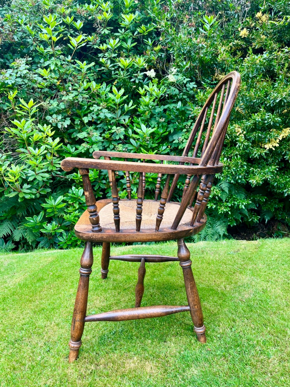 An antique ash Windsor armchair featuring a hoop back with vertical spindles, curved armrests, a woven rush seat, and turned legs linked by stretchers. View VII