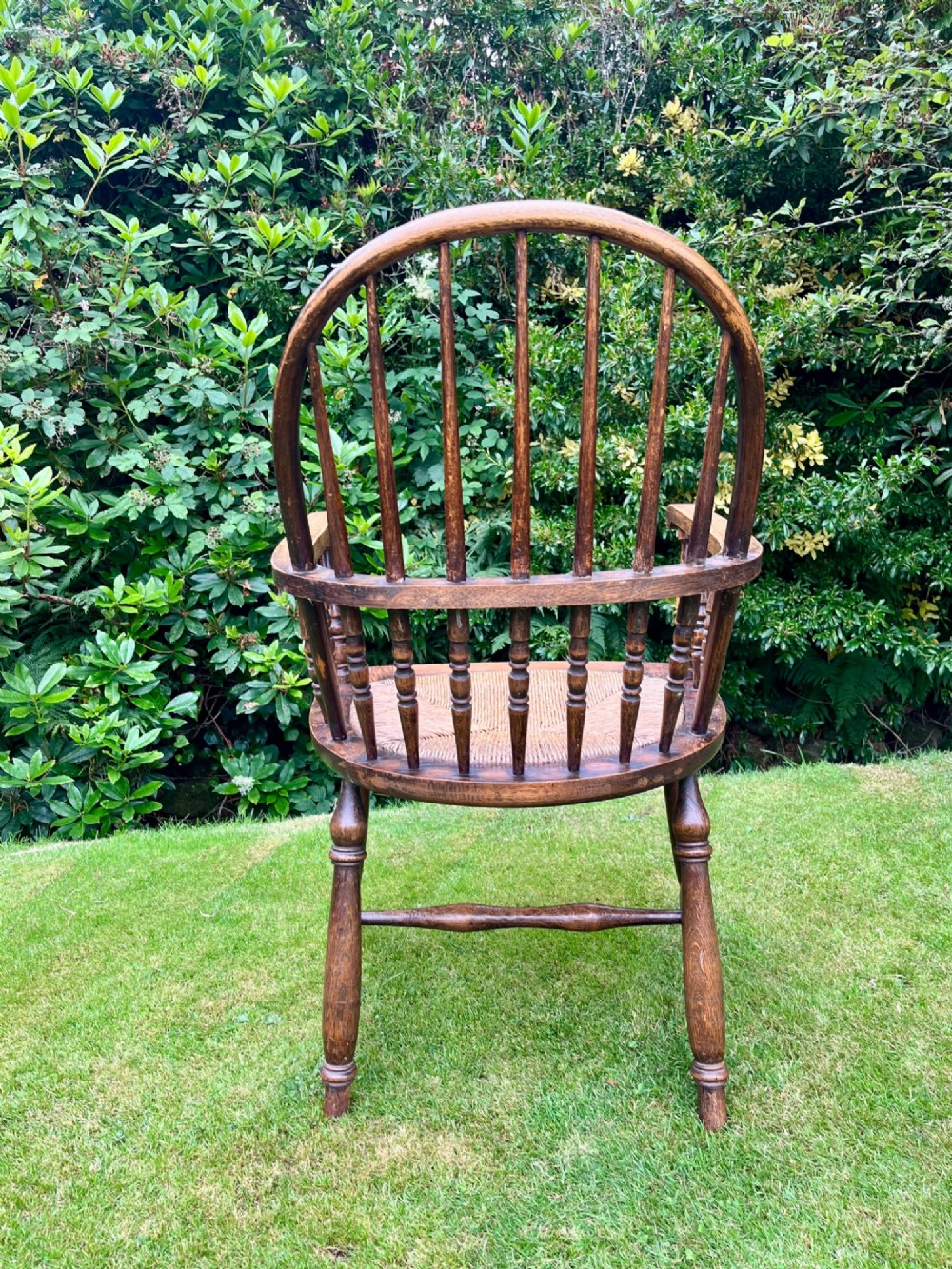 An antique ash Windsor armchair featuring a hoop back with vertical spindles, curved armrests, a woven rush seat, and turned legs linked by stretchers. View VIII