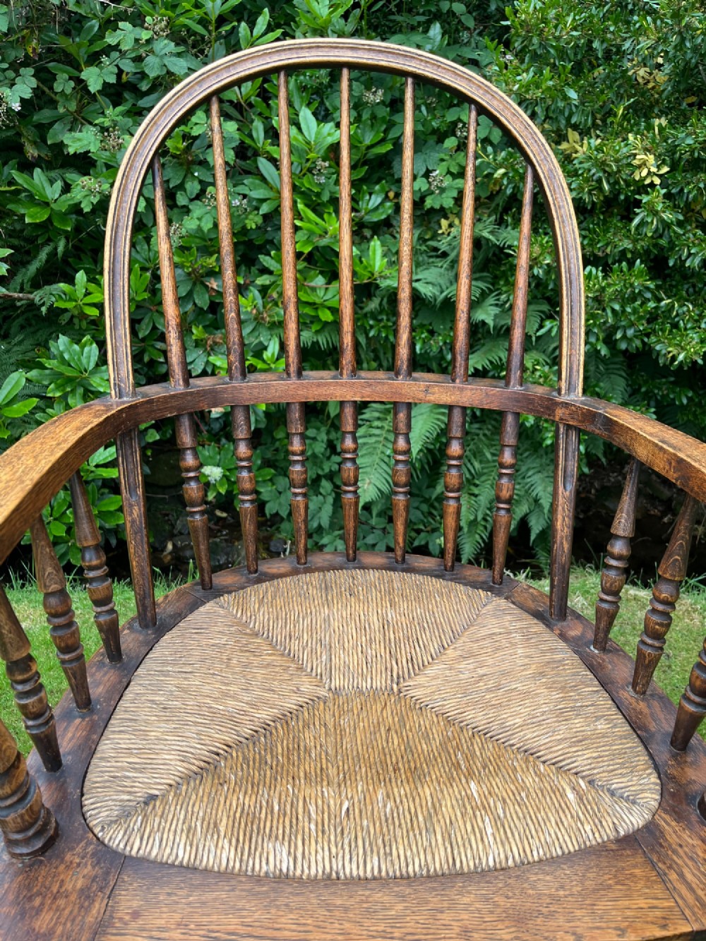An antique ash Windsor armchair featuring a hoop back with vertical spindles, curved armrests, a woven rush seat, and turned legs linked by stretchers. View IX