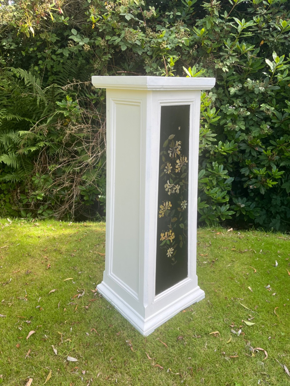 A pair of white wooden tapered display pedestals with inset black panels decorated with hand-painted floral and botanical foliage designs. View III