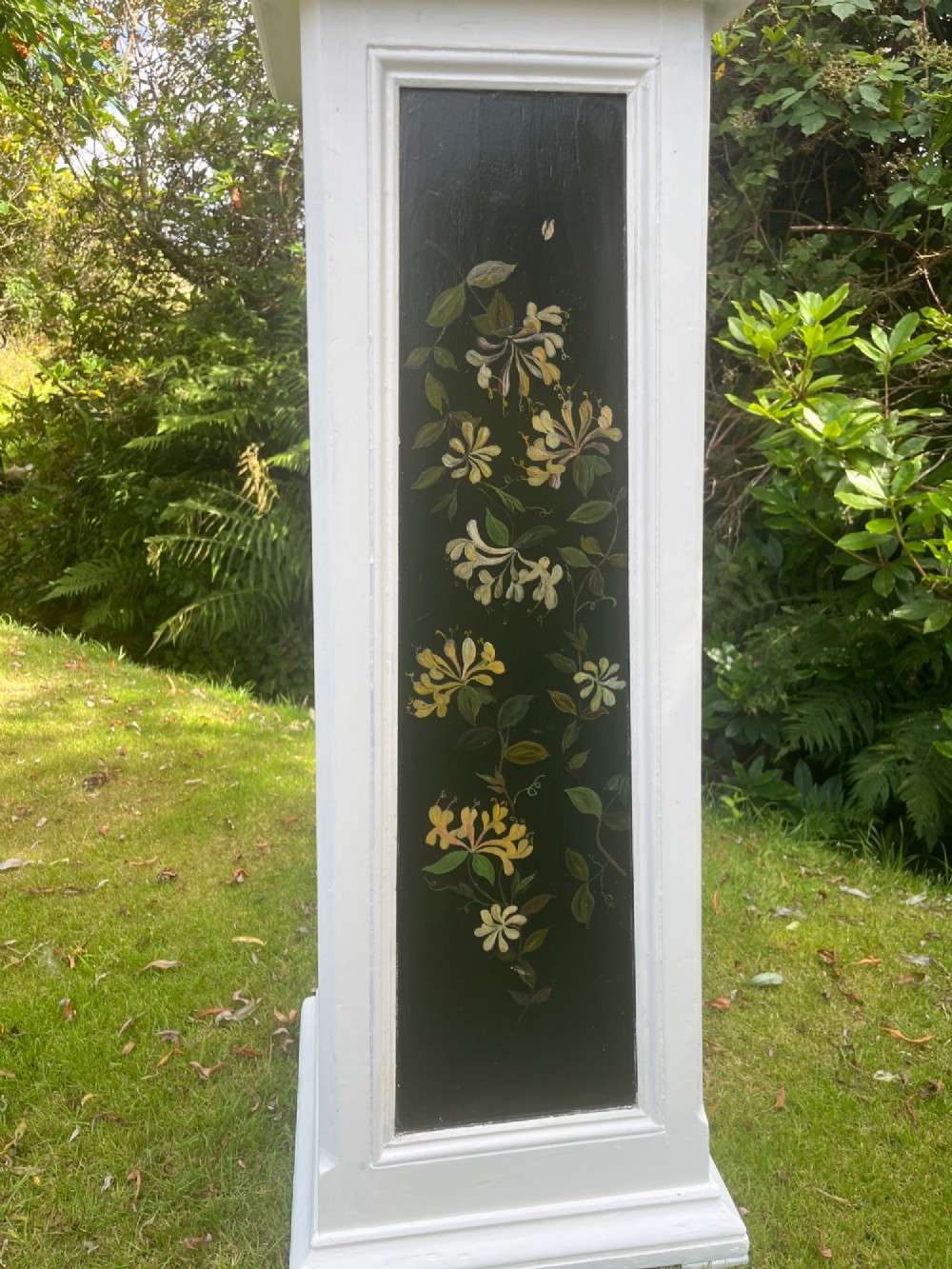 A pair of white wooden tapered display pedestals with inset black panels decorated with hand-painted floral and botanical foliage designs. View V