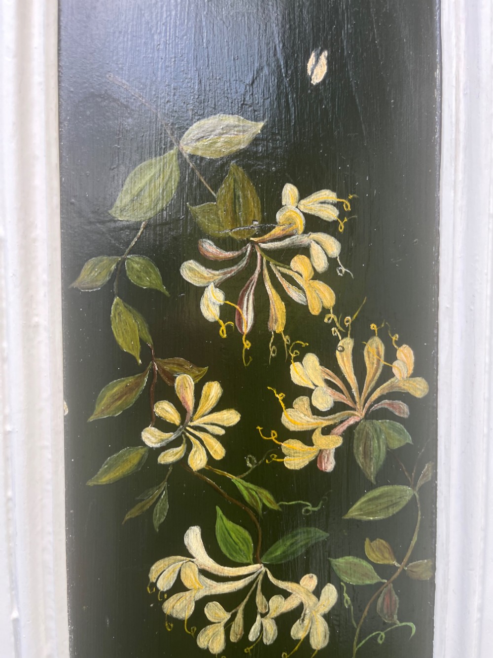 A pair of white wooden tapered display pedestals with inset black panels decorated with hand-painted floral and botanical foliage designs. View VII