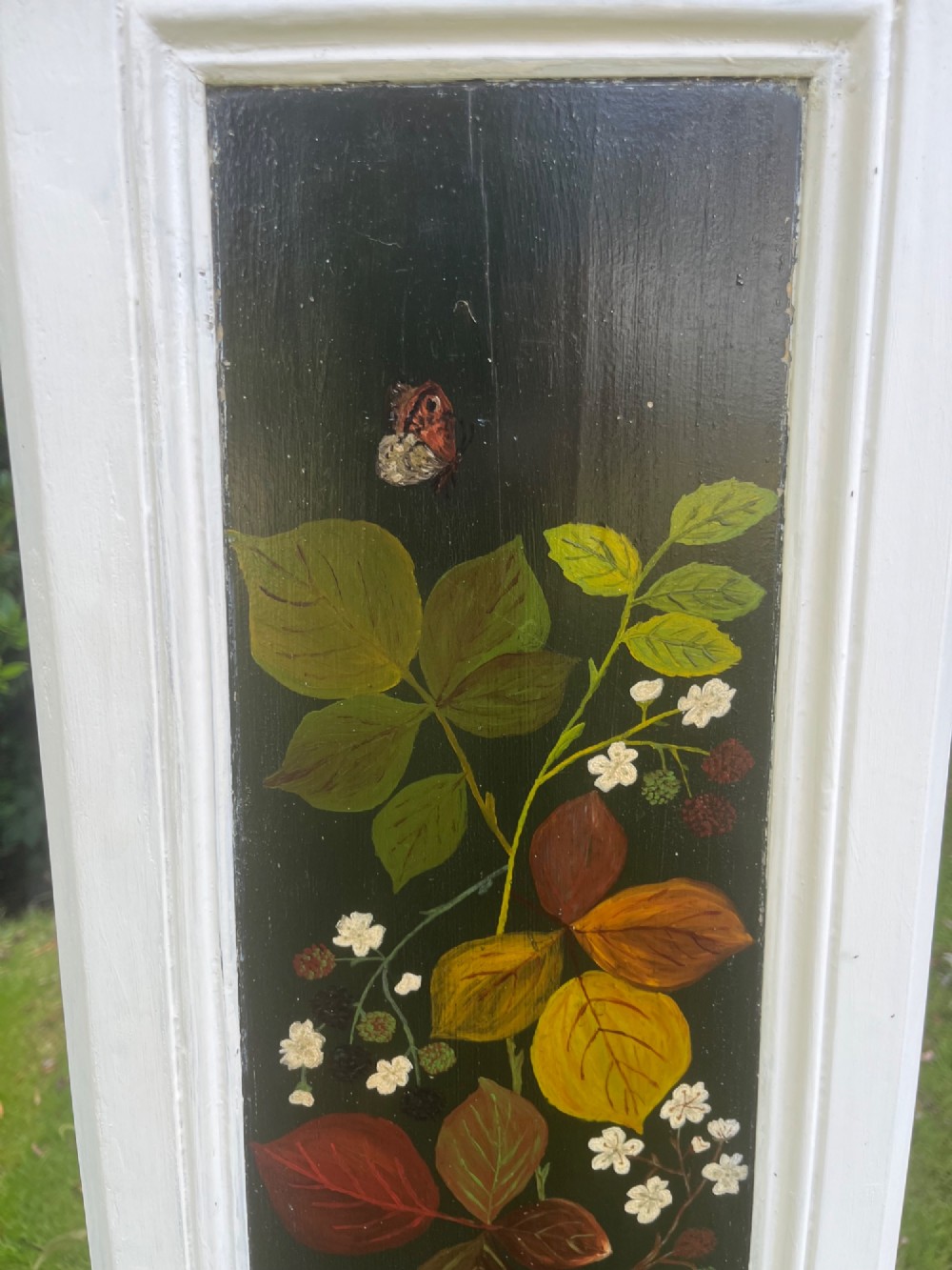 A pair of white wooden tapered display pedestals with inset black panels decorated with hand-painted floral and botanical foliage designs. View X