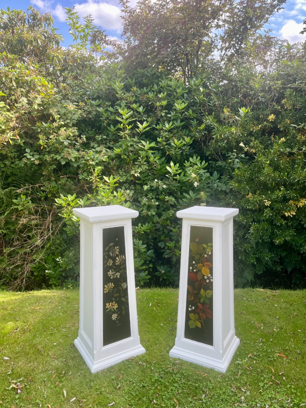 A pair of white wooden tapered display pedestals with inset black panels decorated with hand-painted floral and botanical foliage designs. View XIV