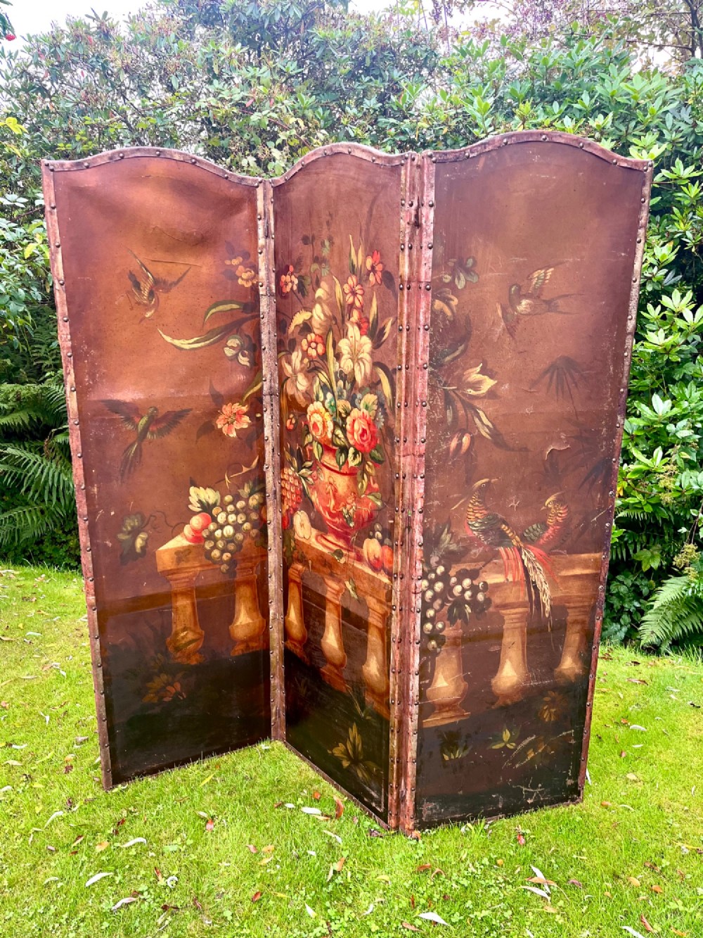 A three-panel antique folding leather screen hand-painted with a central urn of flowers, fruit, and exotic birds against a warm brown background. View X